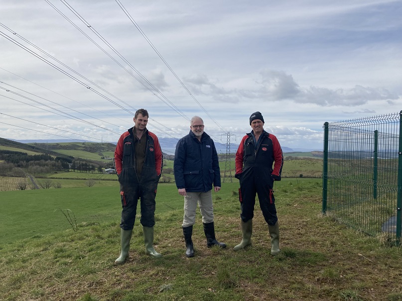 Three men stood in a field with powerlines overhead